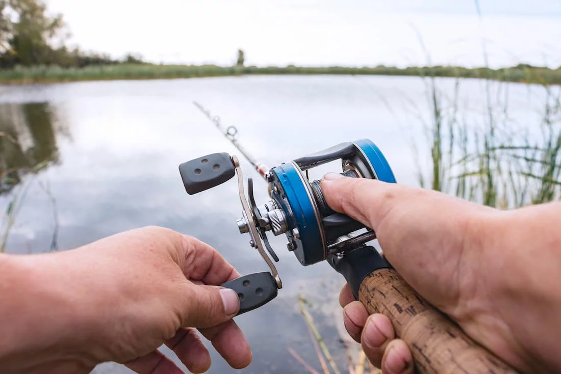 Man using a baitcasting reel at a lake.