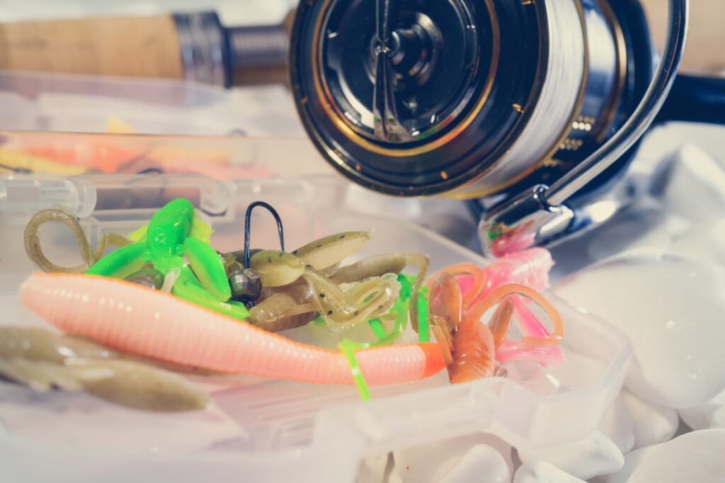 Fishing reel next to jigs and trailers.