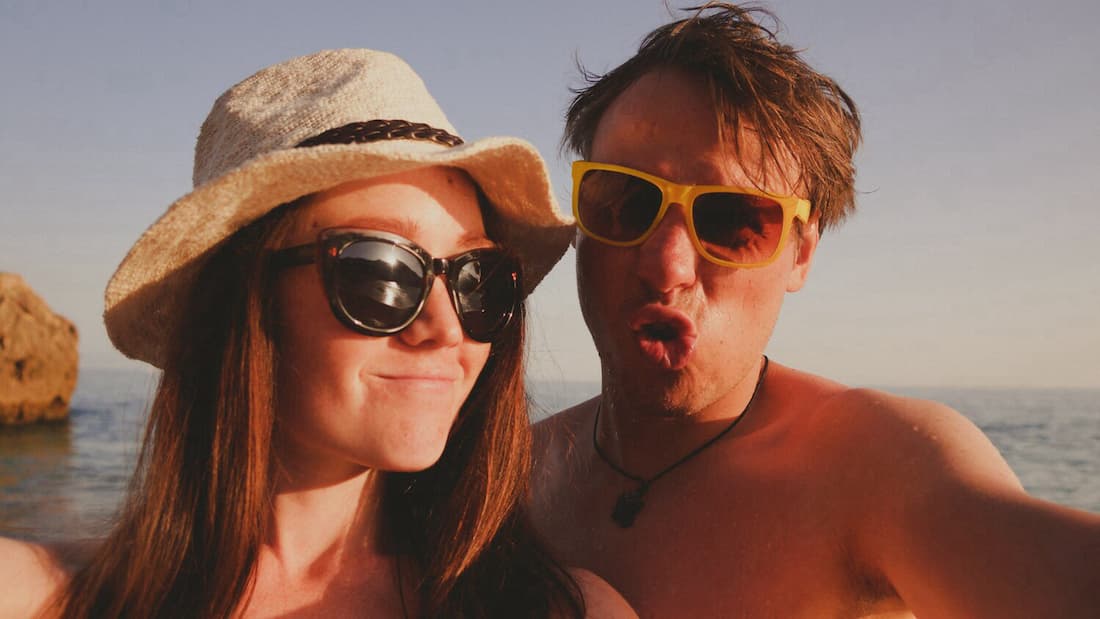 Woman and man posing on beach wearing sunglasses