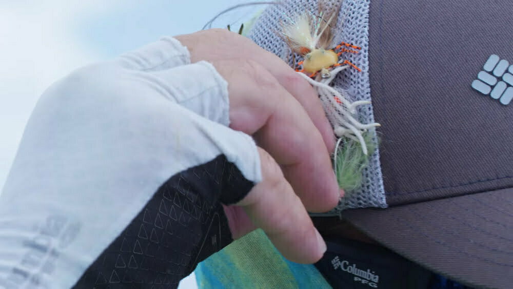 Man is wearing fishing gloves while getting a lure from his hat