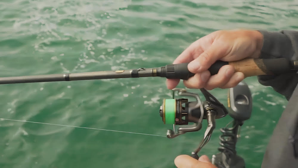 Dangling a Lews Custom Pro Spinning Reel off a hand holding a water bottle.