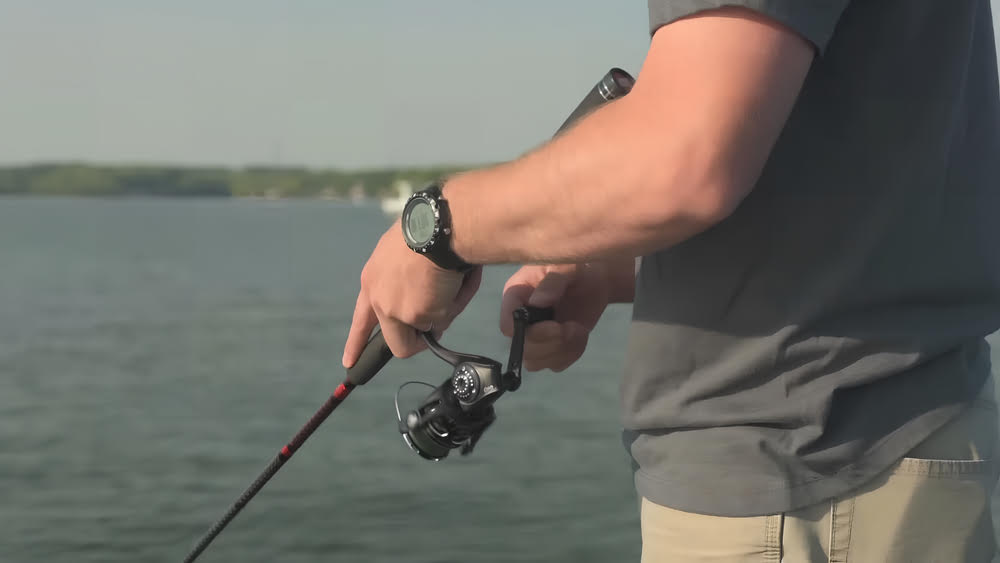 A man standing in the lake with an Abu Garcia Revo MGX Spinning Reel in his hands.