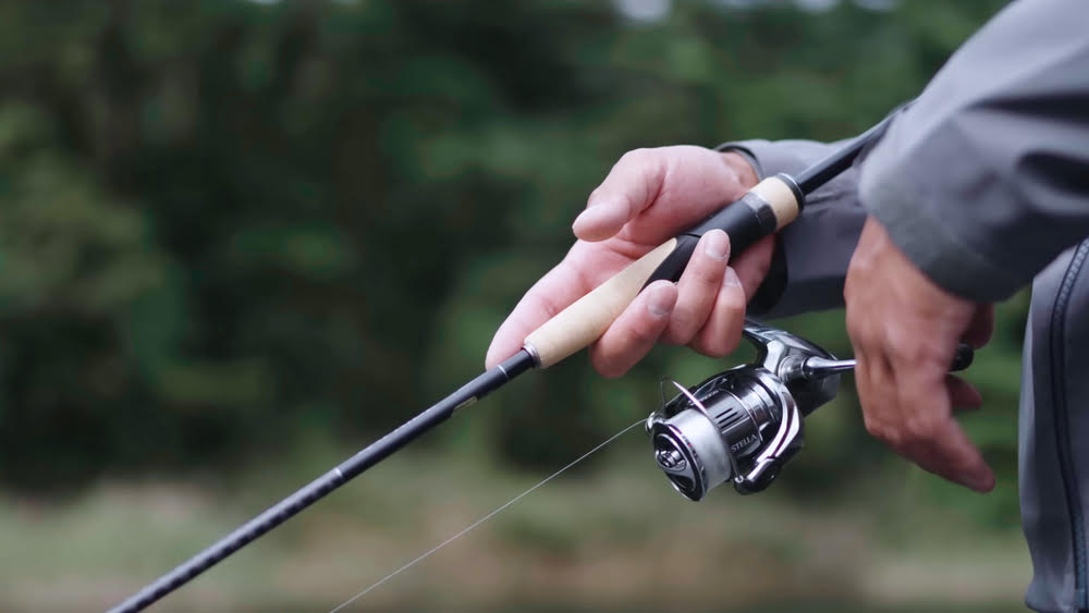 Hands holding a Stella FK Spinning Reel fishing reel.