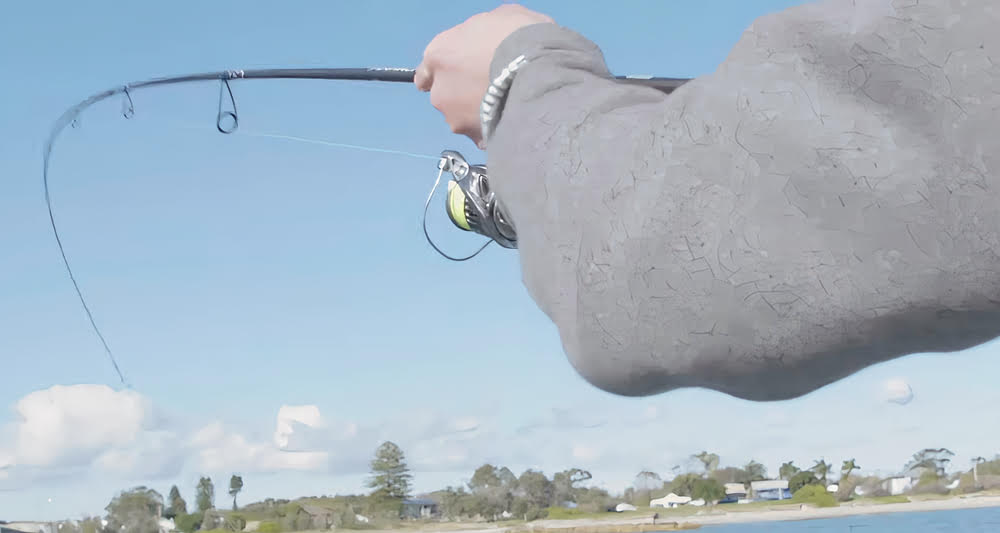 Hands gripping the Shimano Nasci FC Spinning Reel while standing near a lake.