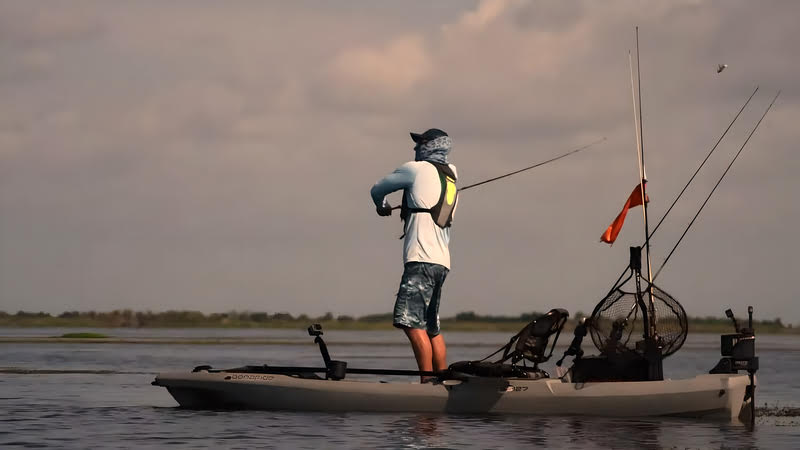 A man standing on a fishing kayak with a fishing rod in his hand